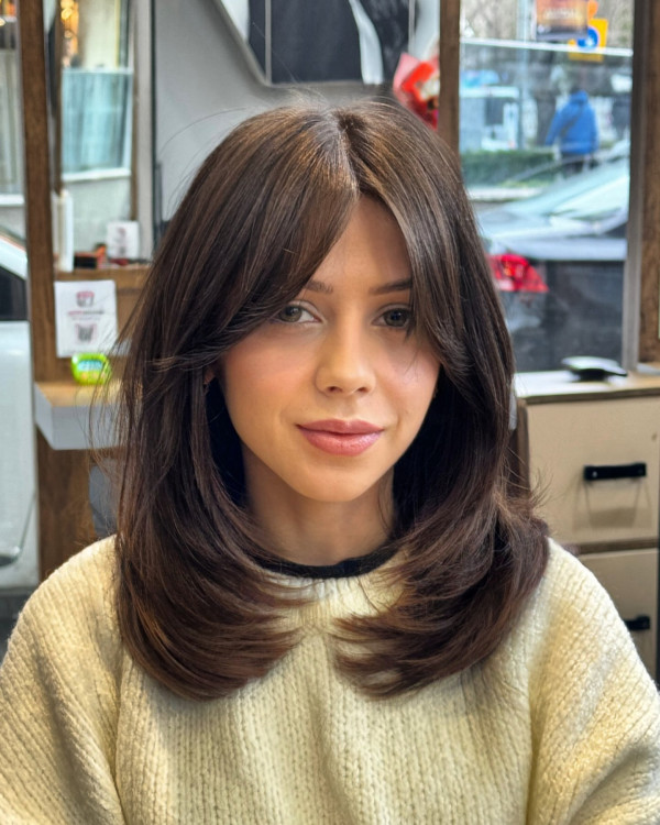 Thick, straight hair with mid-length layers and curtain bangs